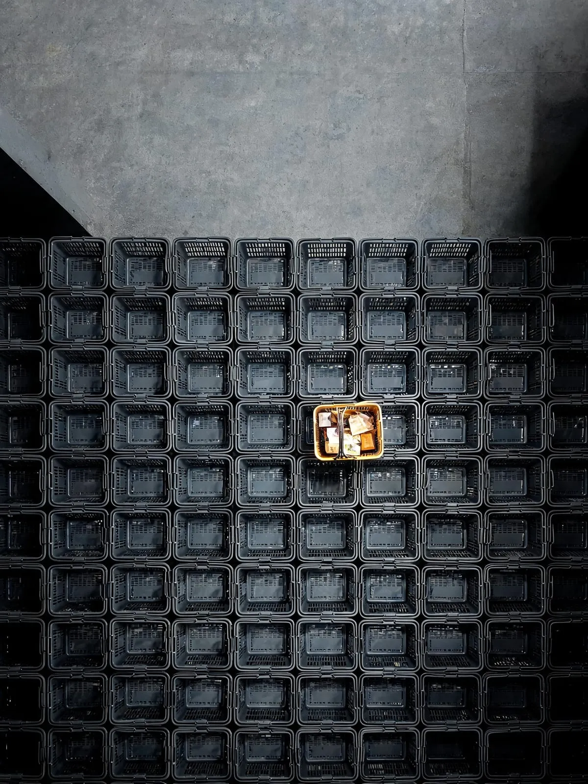 Overhead photograph of hundreds of identical grey shopping baskets in a grid, with one basket lifted and lit gold as the only full one, representing the small share of AI-referred retail traffic that carries most of the value.